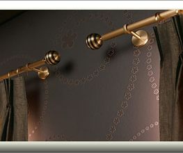 Goldene Vorhangstange mit braunen Vorhängen vor einer dunkelgrauen gemusterten Wand.
