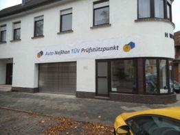 Gebäude mit Schild "Auto Naßhan TÜV Prüfstützpunkt", gelbes Auto im Vordergrund.