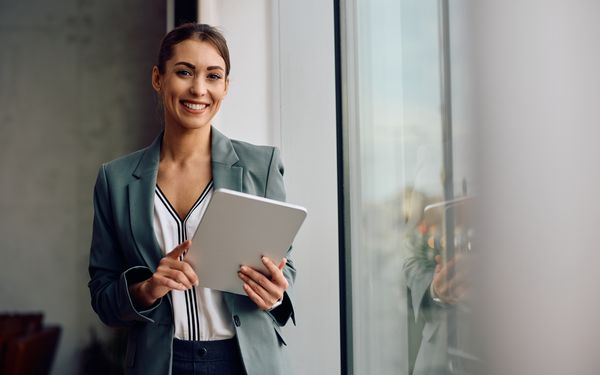 Glückliche Geschäftsfrau, die auf einem digitalen Tablet im Büro arbeitet und in die Kamera schaut.