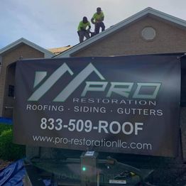 Two workers on a roof, large banner for Pro Restoration in the foreground.