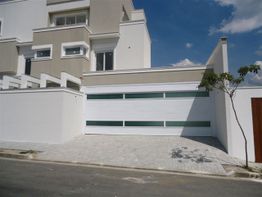 Casa moderna, fachada branca e bege, com porta de garagem seccional ampla. Céu azul ao fundo.
