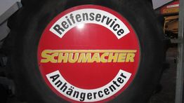 Reifen mit Aufschrift "Reifenservice Anhängercenter Schumacher" auf rotem Hintergrund.