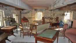 Antiker Raum mit Holzmöbeln und Kronleuchtern, Ziegelwände und Dachbalken sichtbar.