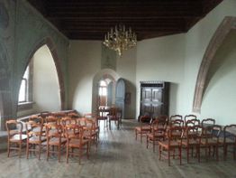 Ein leerer Raum mit Holzstühlen, Schrank, Kronleuchter und Gewölbedecke.