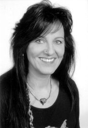 Eine Frau mit langen Haaren lächelt in die Kamera, in Schwarz-Weiß aufgenommen.