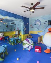 Sala de juegos infantil con temática marina, juguetes, mesas y un gran pingüino de peluche.