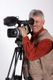 Ein lächelnder Mann filmt mit einer großen Videokamera auf einem Stativ.