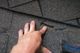 Hand examining damaged roof shingle with a visible tear.