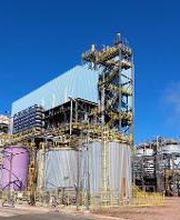 Usina industrial com tanques e estrutura metálica sob céu azul claro.