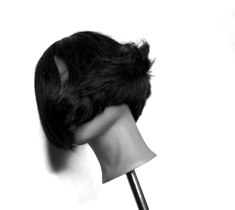 Manichino con capelli scuri e corti, inclinato su un lato, su sfondo bianco.