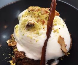 Postre de helado sobre brownie, decorado con nueces y caramelo en un plato negro.