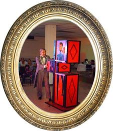 Ilusionista en traje realiza un truco con una caja mágica durante un evento, enmarcado.