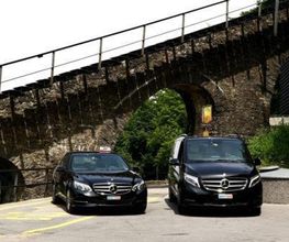 Zwei schwarze Mercedes-Taxis stehen unter einem steinernen Viadukt auf einer Straße.