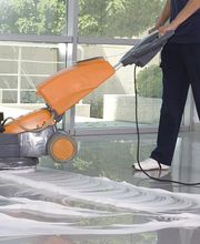 Person reinigt den Boden mit einer Maschine, Wasser und Reinigungsmittel im Vordergrund.