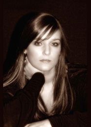 Frau mit langem Haar, ernstem Gesichtsausdruck, stützt Kopf auf Hand vor dunklem Hintergrund.