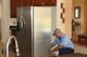 Person fixing a stainless steel refrigerator in a kitchen setting.