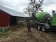 Concrete truck unloading at a construction site beside a red barn structure.
