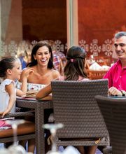 Familia sonriente sentada en una terraza, disfrutando de una comida juntos al aire libre.