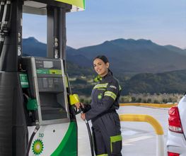 Mujer surtiendo gasolina en estación BP con montañas al fondo.