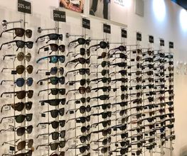 Fila de gafas de sol exhibidas en una pared de una tienda, con descuentos del 20%.
