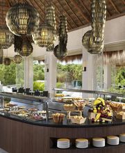Mesa de buffet en un restaurante con lámparas colgantes y ventanas al exterior.