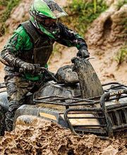 Persona conduciendo un quad cubierto de lodo en un terreno embarrado.