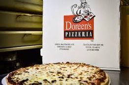 Pizza with cheese and toppings in front of a Doreen's Pizzeria box.