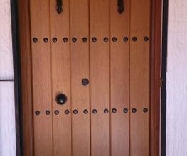Puerta de madera estilo rústico con clavos de hierro negros y arco superior decorativo.
