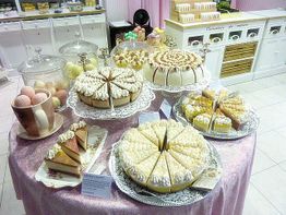 Ein Tisch mit verschiedenen Kuchen und Torten in einer Konditorei auf rosa Tischdecke.