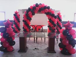 Arco de globos rojos y negros sobre mesa de cristal con sillas, decorado con columnas de globos.