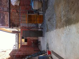 Cortile in costruzione con mattoni rossi, impalcatura e attrezzature da lavoro sparse sul suolo.