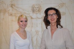 Zwei Frauen stehen vor einer Abbildung von Da Vincis Vitruvianischem Menschen.