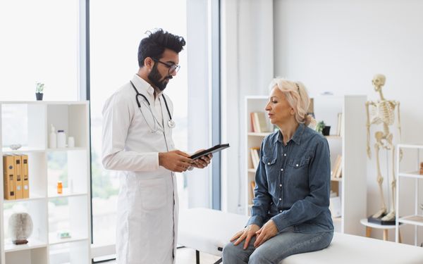 Mitarbeiterin sitzt auf einer Behandlungsliege und spricht mit dem betrieblichen Physiotherapeuten über ihre Beahndlung.