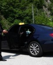 Ein Mann im Anzug öffnet die Tür eines schwarzen Autos mit Taxischild.