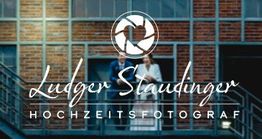 Ein Paar steht auf einer Treppe vor einem Gebäude. Text: Ludger Staudinger Hochzeitsfotograf.