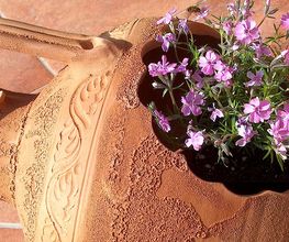 Vaso di terracotta decorato con fiori rosa, su un pavimento di piastrelle marroni.