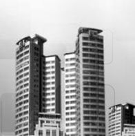 Drei moderne Hochhäuser vor bewölktem Himmel, in Schwarzweißaufnahme.