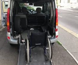Rollstuhl auf einer Rampe im Kofferraum eines Autos neben einer Straße.