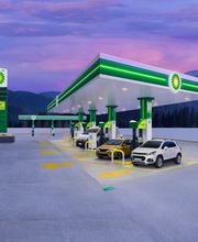 Estación de servicio BP iluminada al atardecer, autos estacionados, con fondo de montañas.