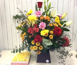 Ramo colorido de flores sobre mesa, con libro amarillo al lado, fondo de madera clara.
