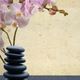 Stacked black stones and pink orchids on a textured background.