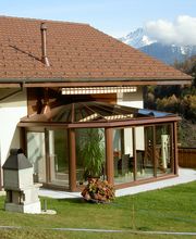 Haus mit Wintergarten im Garten, Berge im Hintergrund.