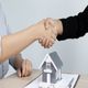 Two people shaking hands over a table with a small house model and keys.