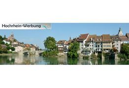 Mittelalterliche Stadt am Fluss mit alten Häusern und Kirchtürmen unter blauem Himmel.