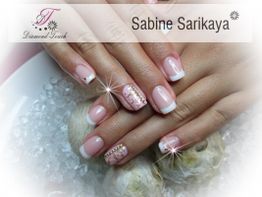 Gepflegte Hände mit French Nails und Verzierungen auf weißen Muscheln.