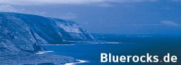 Küste mit hohen Klippen bei blauem Meer; Schriftzug "Bluerocks.de" unten rechts.