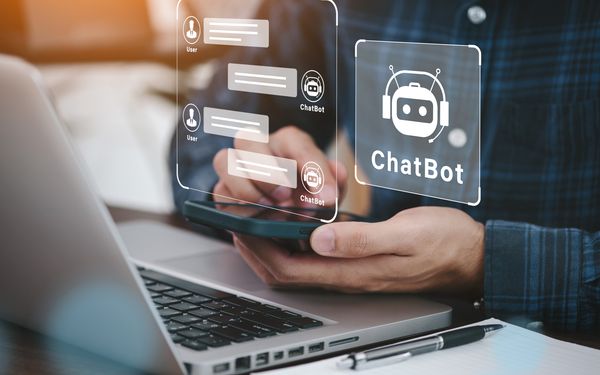 Mann mit Handy in der Hand kommuniziert mit dem KI-Chatbot eines Kundenservices. Der KI-Chatbot wird als Grafik dargestellt.