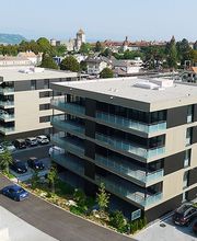 Moderne Wohngebäude mit Balkon vor Stadtansicht und grüner Landschaft im Hintergrund.