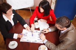 Three people having a meeting at a round table with documents and coffee.
