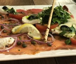 Teller mit Carpaccio, Mozzarella, Tomaten, Rucola, Zwiebeln, Kapern und Zitronenscheiben.